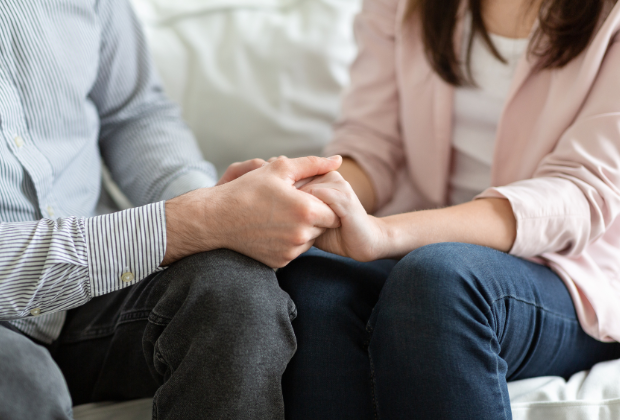 Close-up of a couple holding hands, signifying support and unity in a therapy session.