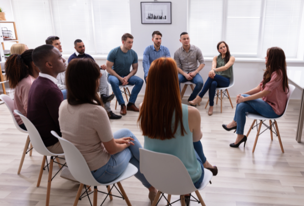 Diverse group of individuals engaged in a group therapy session seated in a circle in a bright, modern room.